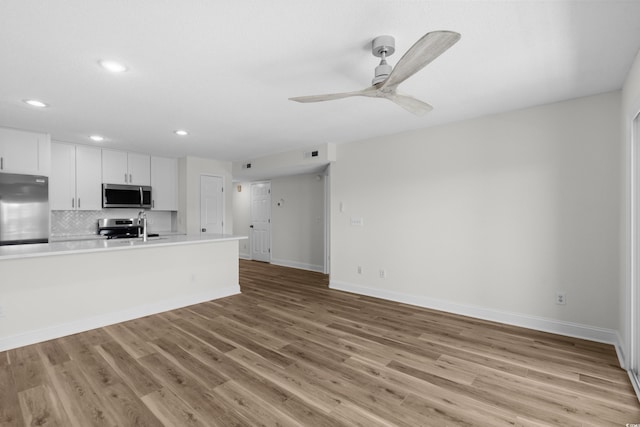 unfurnished living room featuring recessed lighting, baseboards, ceiling fan, light wood-style flooring, and a sink