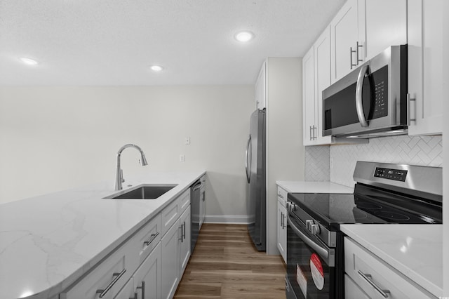 kitchen featuring appliances with stainless steel finishes, a sink, wood finished floors, baseboards, and backsplash