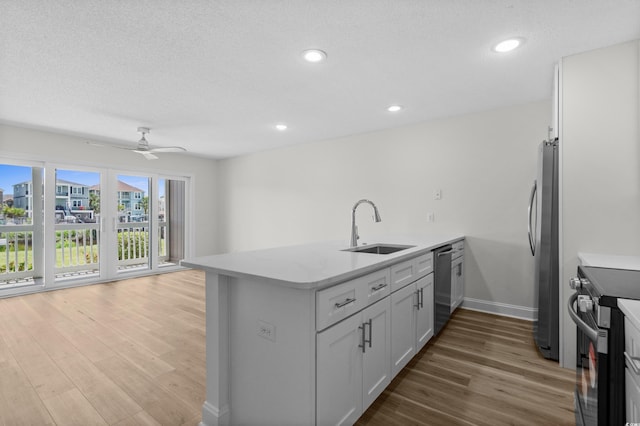 kitchen featuring stainless steel appliances, a sink, a peninsula, light wood-style floors, and ceiling fan