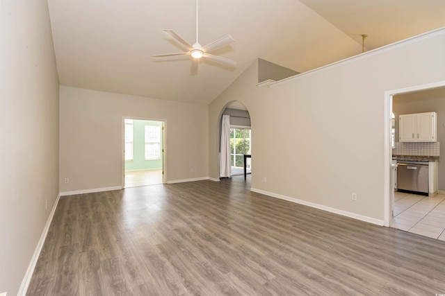 empty room with arched walkways, a ceiling fan, high vaulted ceiling, light wood-style floors, and baseboards