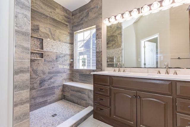 bathroom with double vanity, a tile shower, and tile patterned flooring