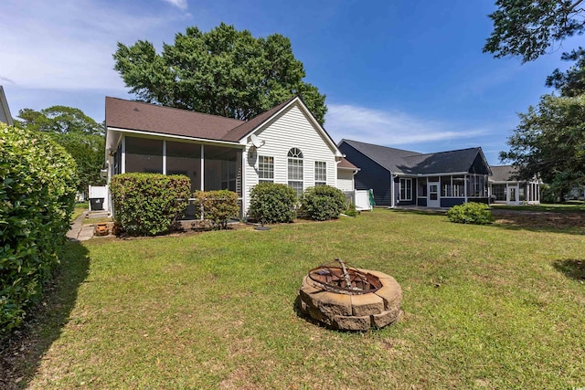 back of house featuring a sunroom, a fire pit, and a lawn