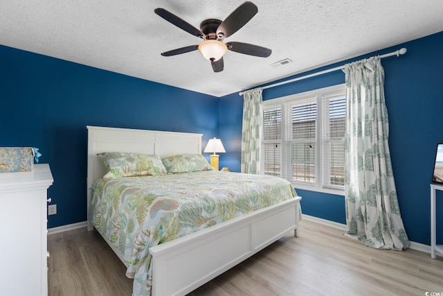 bedroom with wood finished floors, baseboards, a ceiling fan, and a textured ceiling