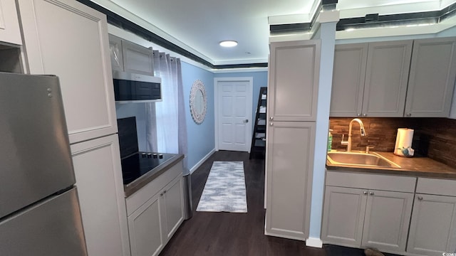 kitchen featuring stainless steel appliances, a sink, dark wood finished floors, tasteful backsplash, and baseboards