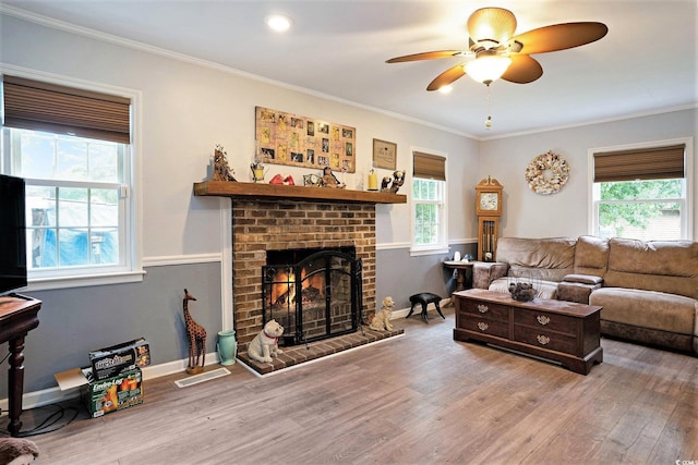 living room with ceiling fan, wood finished floors, a fireplace, crown molding, and baseboards