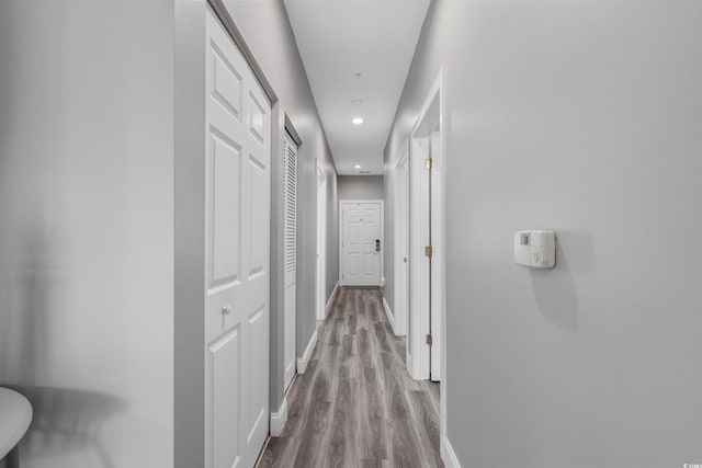 hall featuring baseboards, wood finished floors, and recessed lighting