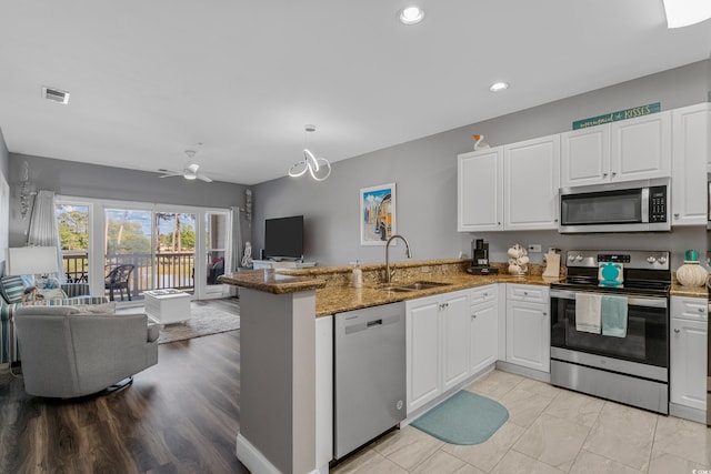 kitchen with appliances with stainless steel finishes, open floor plan, a peninsula, a sink, and white cabinets