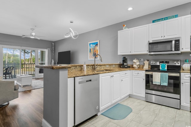 kitchen featuring appliances with stainless steel finishes, a sink, a peninsula, open floor plan, and white cabinets