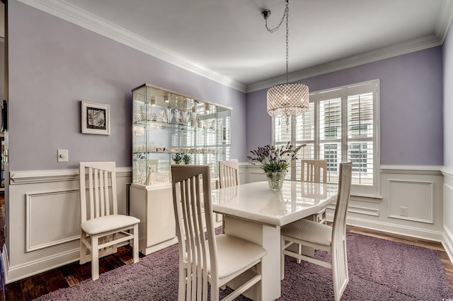 dining room with wood finished floors, wainscoting, ornamental molding, a chandelier, and a decorative wall