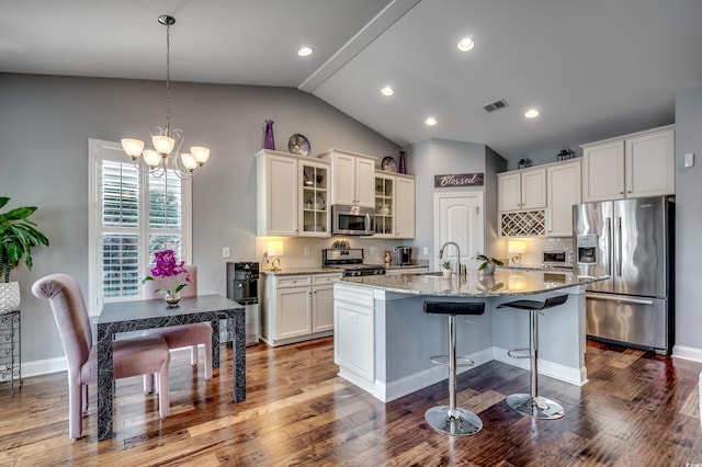 kitchen featuring appliances with stainless steel finishes, vaulted ceiling, white cabinetry, a chandelier, and an island with sink