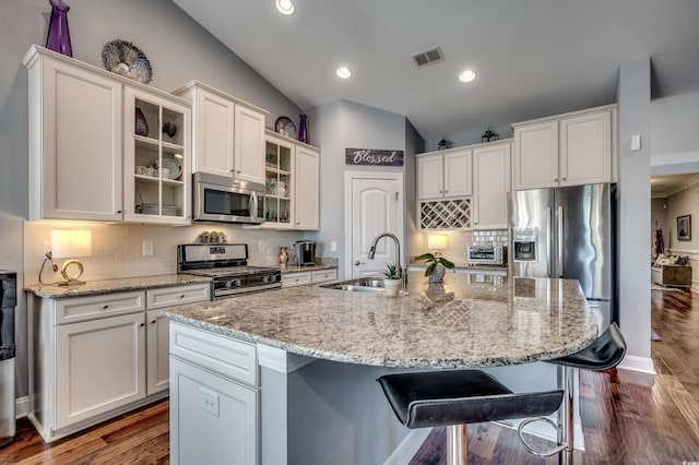 kitchen featuring appliances with stainless steel finishes, a sink, vaulted ceiling, tasteful backsplash, and white cabinetry