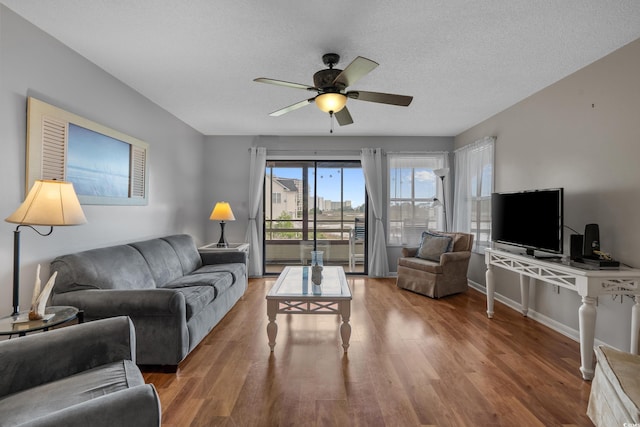 living area with a ceiling fan, wood finished floors, baseboards, and a textured ceiling
