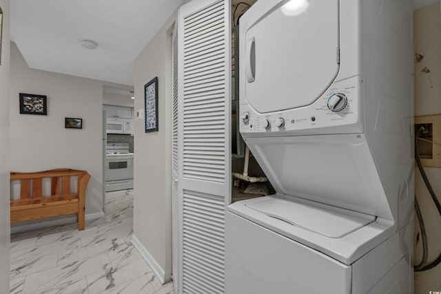 laundry area featuring stacked washer / dryer, light marble finish flooring, and baseboards