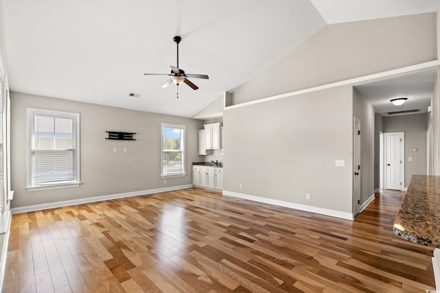unfurnished living room with a ceiling fan, light wood-style flooring, high vaulted ceiling, and baseboards