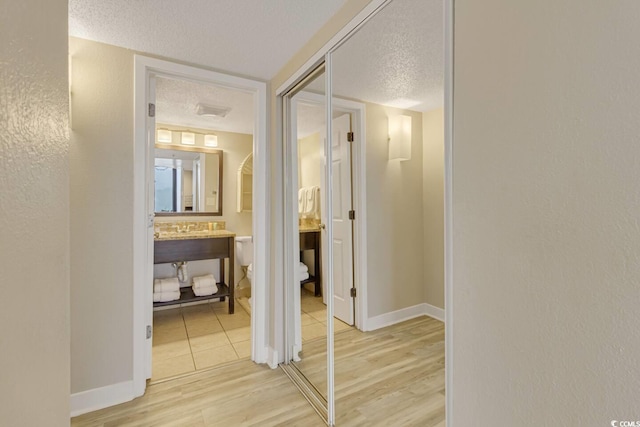 hallway featuring a textured ceiling, light wood finished floors, and baseboards