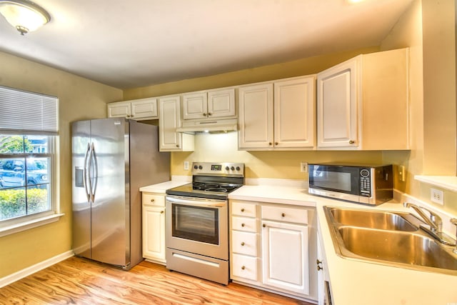 kitchen with appliances with stainless steel finishes, a sink, under cabinet range hood, light wood-type flooring, and light countertops