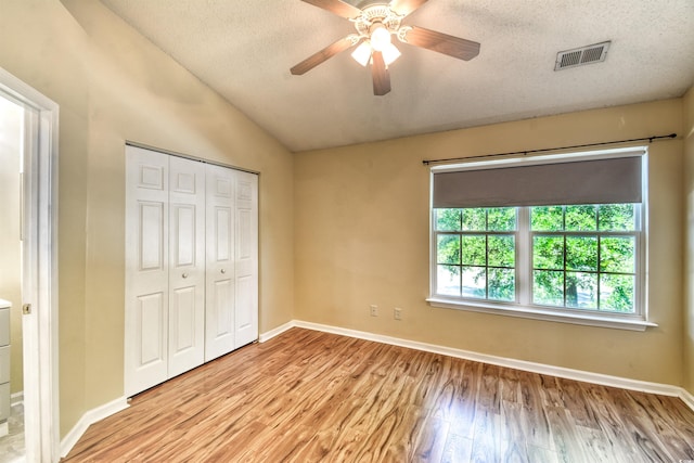 unfurnished bedroom featuring light wood-type flooring, a closet, lofted ceiling, baseboards, and a textured ceiling