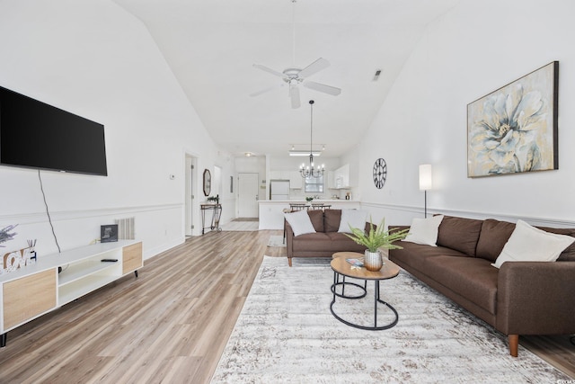 living area with high vaulted ceiling, light wood-style flooring, a ceiling fan, and a chandelier