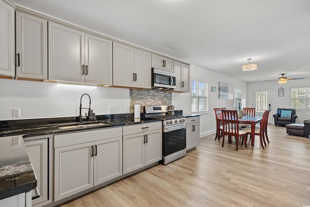 kitchen featuring appliances with stainless steel finishes, a sink, light wood finished floors, open floor plan, and a ceiling fan