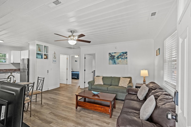 living area with light wood finished floors, crown molding, ceiling fan, and baseboards