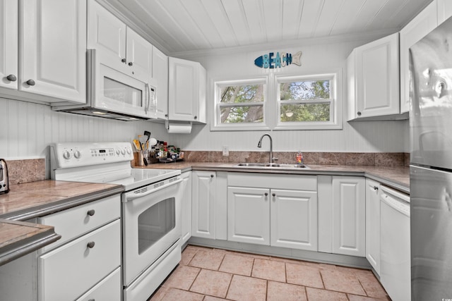 kitchen with white appliances, a sink, white cabinets, light stone finish floors, and ornamental molding