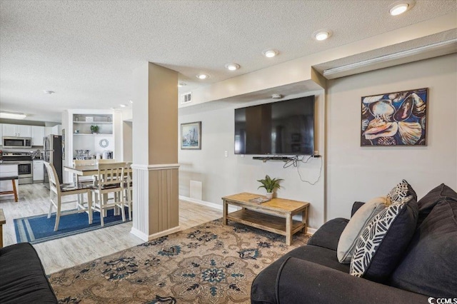 living room with light wood finished floors, a textured ceiling, recessed lighting, decorative columns, and baseboards