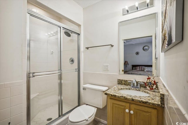 ensuite bathroom with tile walls, a stall shower, toilet, a wainscoted wall, and vanity