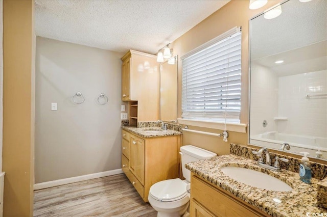 full bathroom featuring toilet, two vanities, a textured ceiling, and wood finished floors