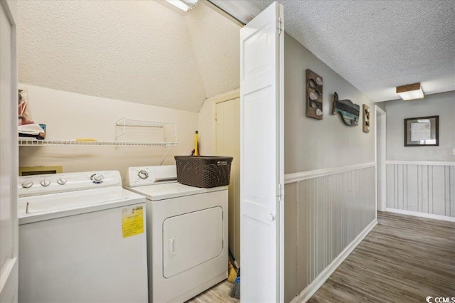 clothes washing area with separate washer and dryer, a textured ceiling, light wood finished floors, and wainscoting