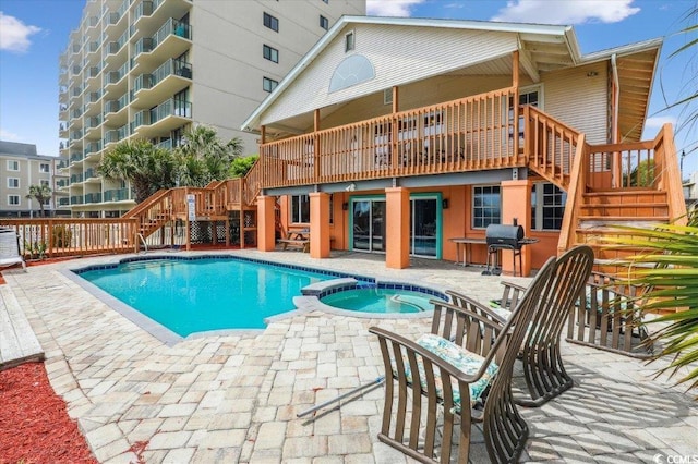 view of swimming pool featuring stairway, a pool with connected hot tub, a patio area, a grill, and a wooden deck