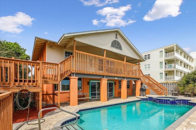 back of house featuring stairs, a wooden deck, a pool with connected hot tub, and a patio area