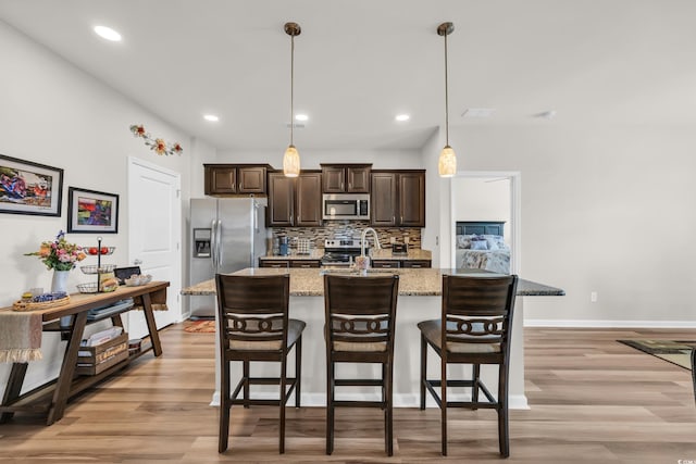 kitchen featuring appliances with stainless steel finishes, dark brown cabinets, a breakfast bar area, light wood-type flooring, and recessed lighting