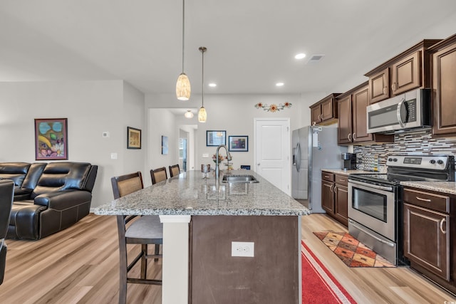 kitchen featuring stainless steel appliances, a sink, a breakfast bar, open floor plan, and light wood-style floors