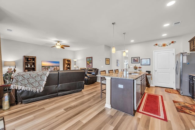 kitchen featuring a sink, a kitchen bar, open floor plan, light wood-style floors, and a ceiling fan