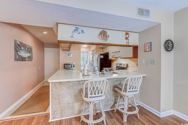 kitchen featuring stainless steel appliances, under cabinet range hood, light wood-style flooring, light countertops, and a textured ceiling