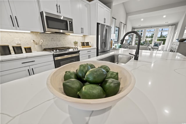 kitchen featuring appliances with stainless steel finishes, a sink, tasteful backsplash, white cabinetry, and light stone counters