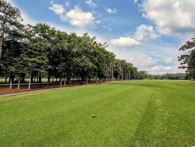 view of home's community featuring view of wooded area, a yard, and view of golf course