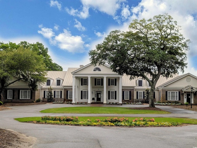 neoclassical home with a standing seam roof, metal roof, curved driveway, and brick siding