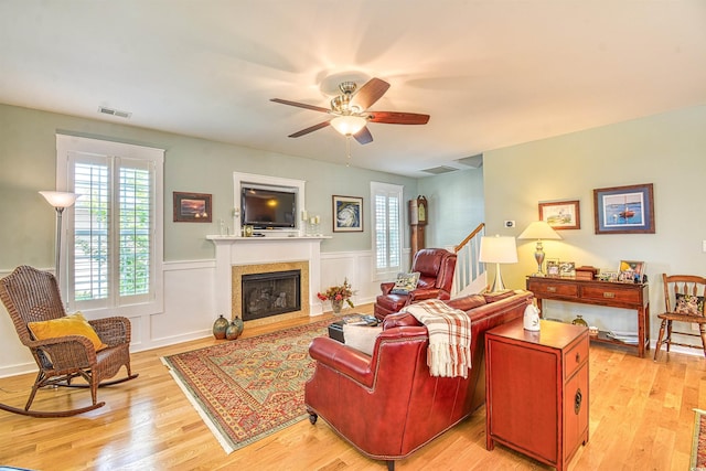 living room with a ceiling fan, wainscoting, light wood finished floors, and a fireplace