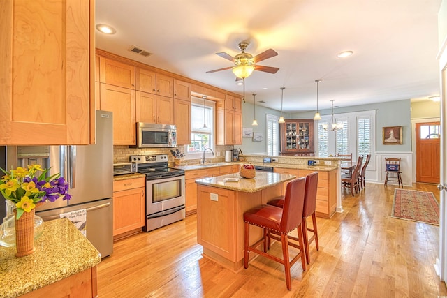 kitchen with stainless steel appliances, a peninsula, a breakfast bar area, light wood-style floors, and a center island