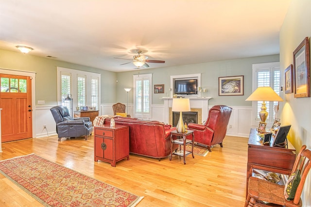 living area with light wood finished floors, plenty of natural light, a fireplace, wainscoting, and a decorative wall