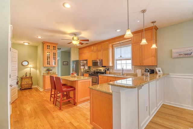 kitchen featuring stainless steel appliances, a sink, a breakfast bar area, light wood-style floors, and a peninsula