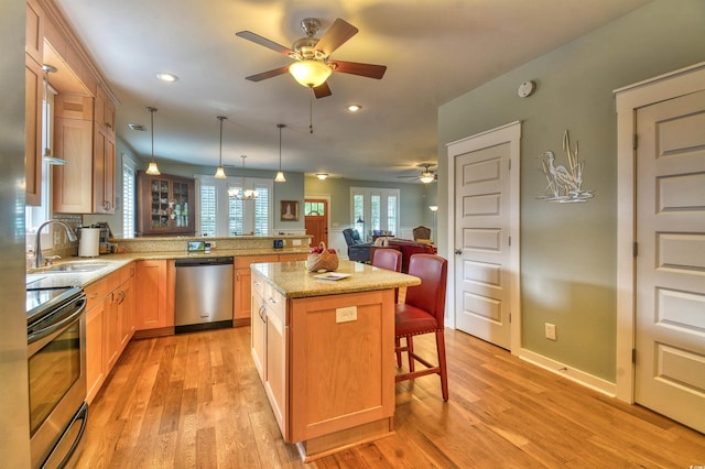 kitchen with appliances with stainless steel finishes, a ceiling fan, a sink, a breakfast bar, and light wood-style flooring