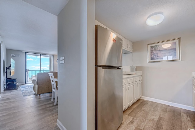 hall with light wood finished floors, baseboards, and a textured ceiling