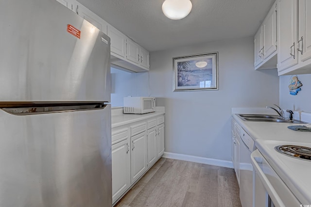 kitchen with white appliances, a sink, light wood finished floors, light countertops, and white cabinetry