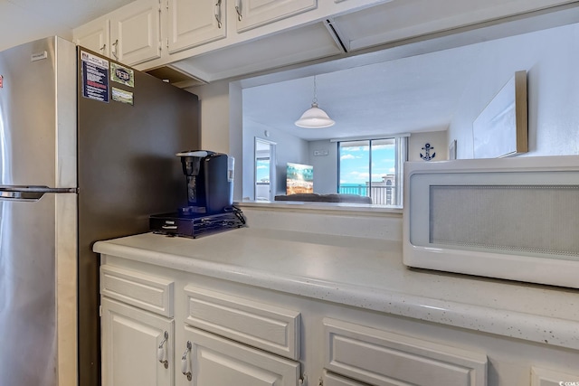 kitchen featuring freestanding refrigerator, white cabinets, light countertops, and hanging light fixtures