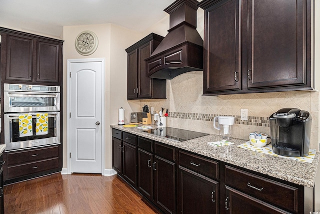 kitchen featuring black electric stovetop, premium range hood, dark wood finished floors, tasteful backsplash, and stainless steel double oven