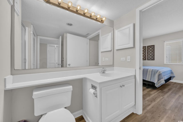 bathroom featuring toilet, wood finished floors, vanity, baseboards, and ensuite bath