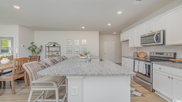 kitchen featuring appliances with stainless steel finishes, a sink, light wood finished floors, white cabinets, and recessed lighting