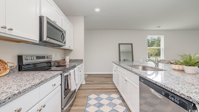 kitchen with stainless steel appliances, a sink, white cabinetry, light wood-style floors, and light stone countertops